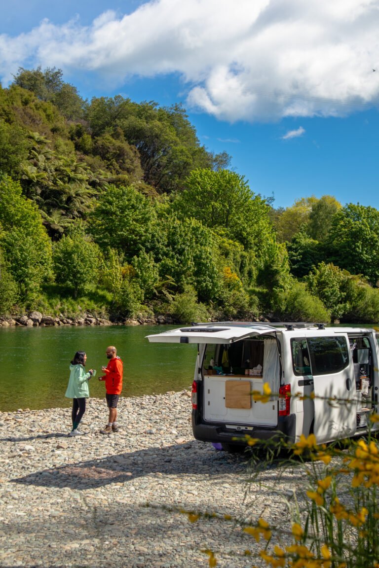 Campervan parked by a river with two people walking along the riverbank in New Zealand
