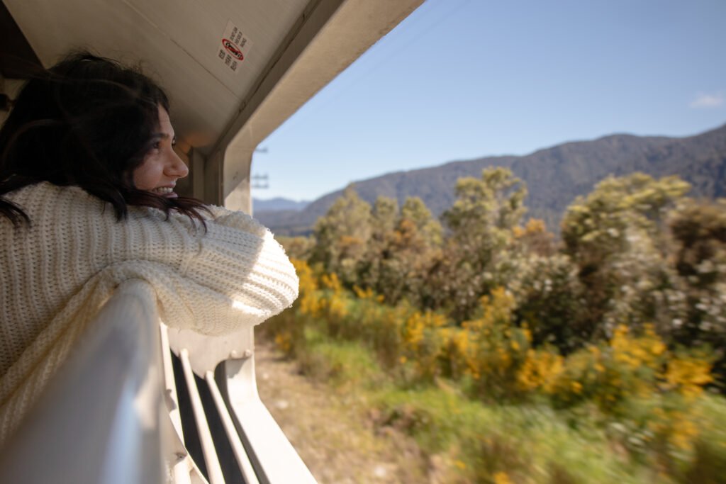 Woman enjoying mountain views from the open carriage on the TranzAlpine scenic train in New Zealand