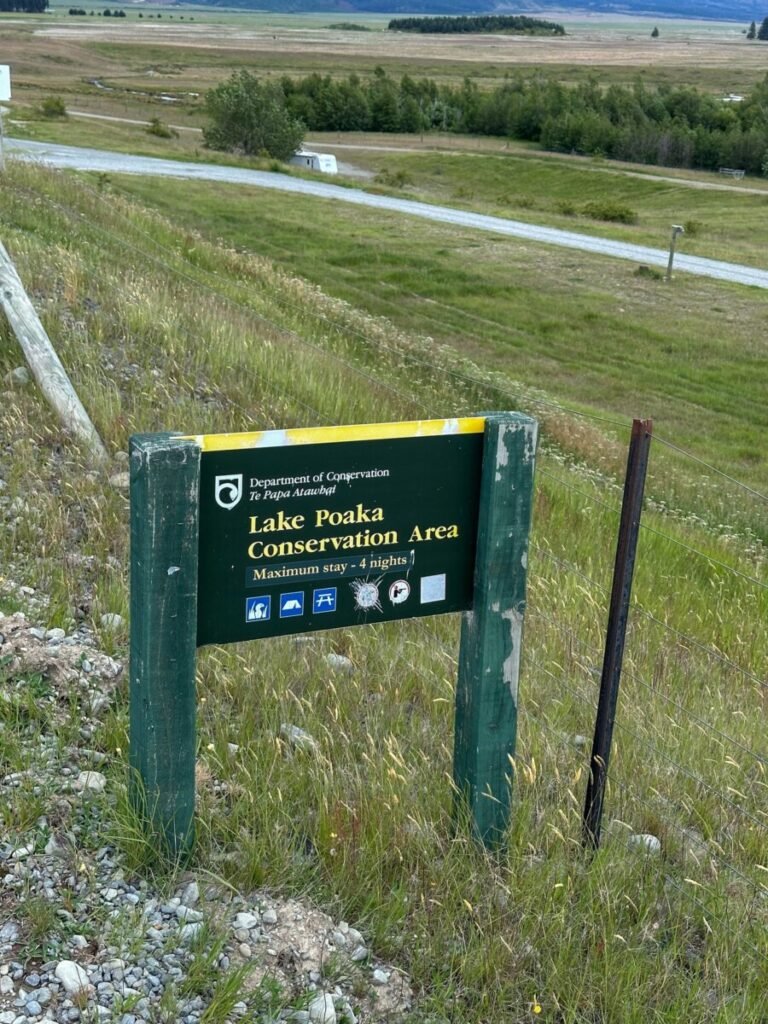 Department of Conservation Lake Poaka Conservation Area sign with campsite rules and grassland in the background McKenzie Region New Zealand