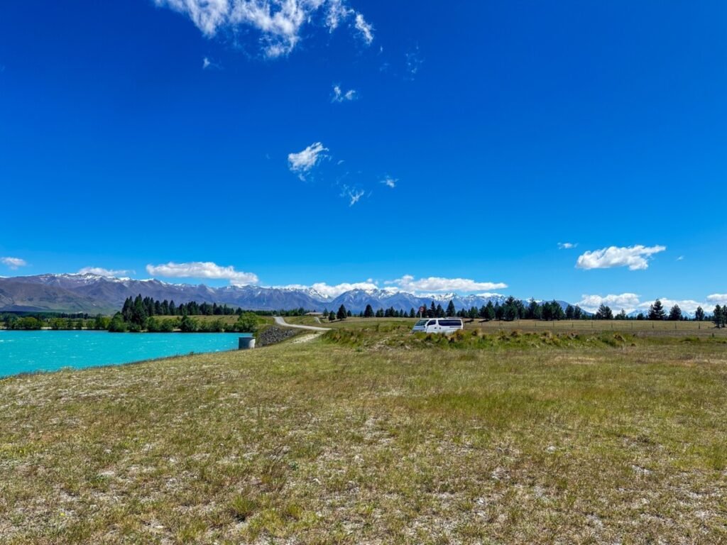 Turquoise blue Lake Pukaki with a white campervan parked along the shore and the Southern Alps visible in the distance McKenzie Region New Zealand