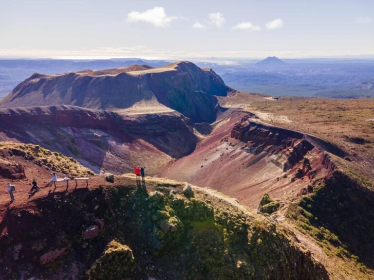 A wide view of a massive volcanic crater fissure with layered red and brown rocky cliffs under a blue sky.