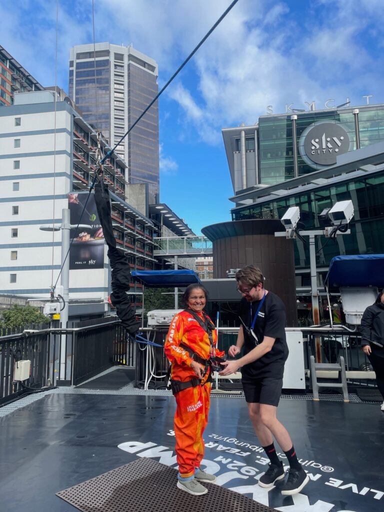 A woman in an orange jumpsuit being fitted with a harness for SkyJump atop Auckland's Sky Tower.